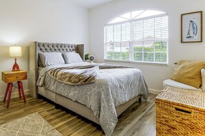 A bedroom with a large bed, a bedside table, a lamp, a window with blinds, and a framed picture on the wall. - Work, Swim + Play in Ft Myers: Resort Condo Stay! (Fort Myers)