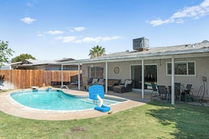 A backyard with a swimming pool, patio furniture, and a covered seating area.