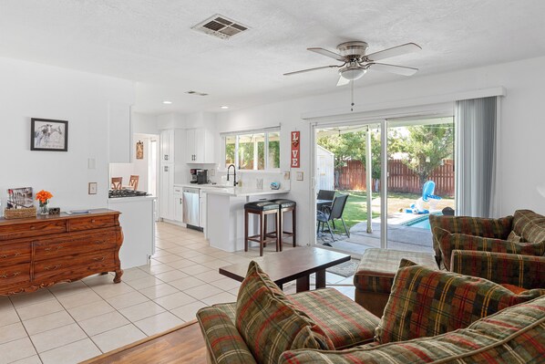 A spacious living room with a plaid sofa, a wooden coffee table, and a kitchen area with white cabinets and a central island.