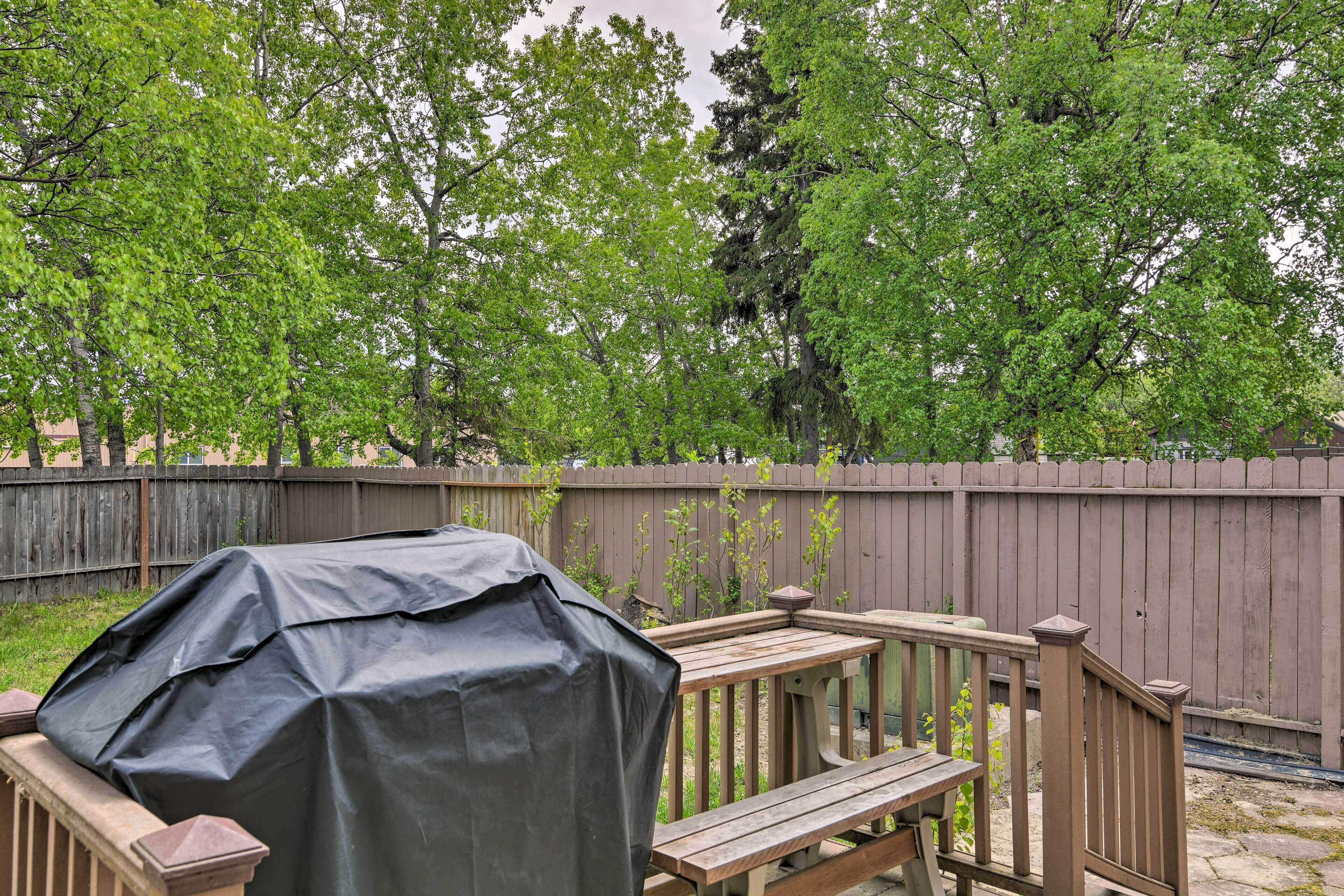 A backyard with a wooden deck, a covered grill, and a wooden table.