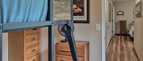 A bunk bed with a wooden dresser, a fan, and a framed picture on the wall.