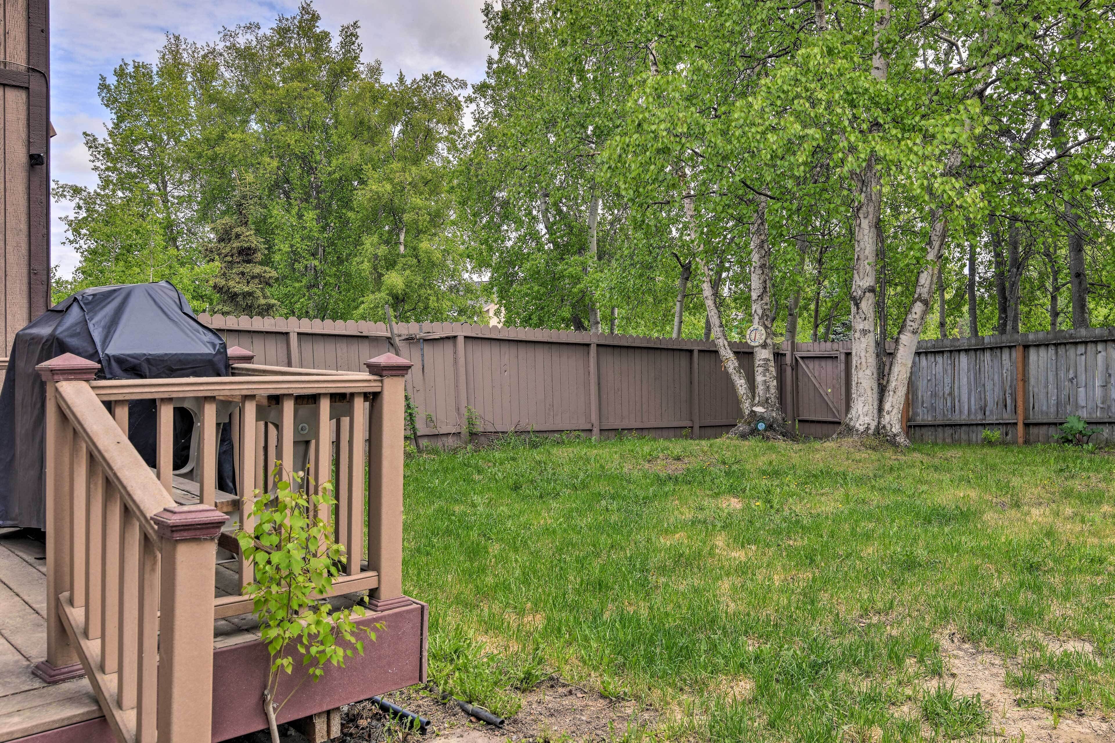 A backyard with a wooden deck, a barbecue grill, and a wooden fence.