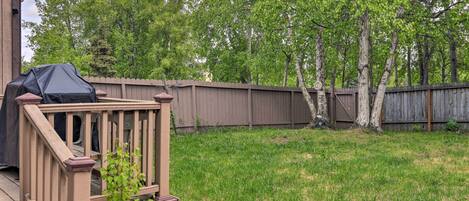 A backyard with a wooden deck, a barbecue grill, and a wooden fence.