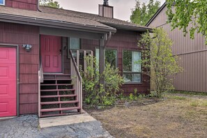 Une maison à deux étages avec une porte rouge, un porche à l’avant et un petit jardin.