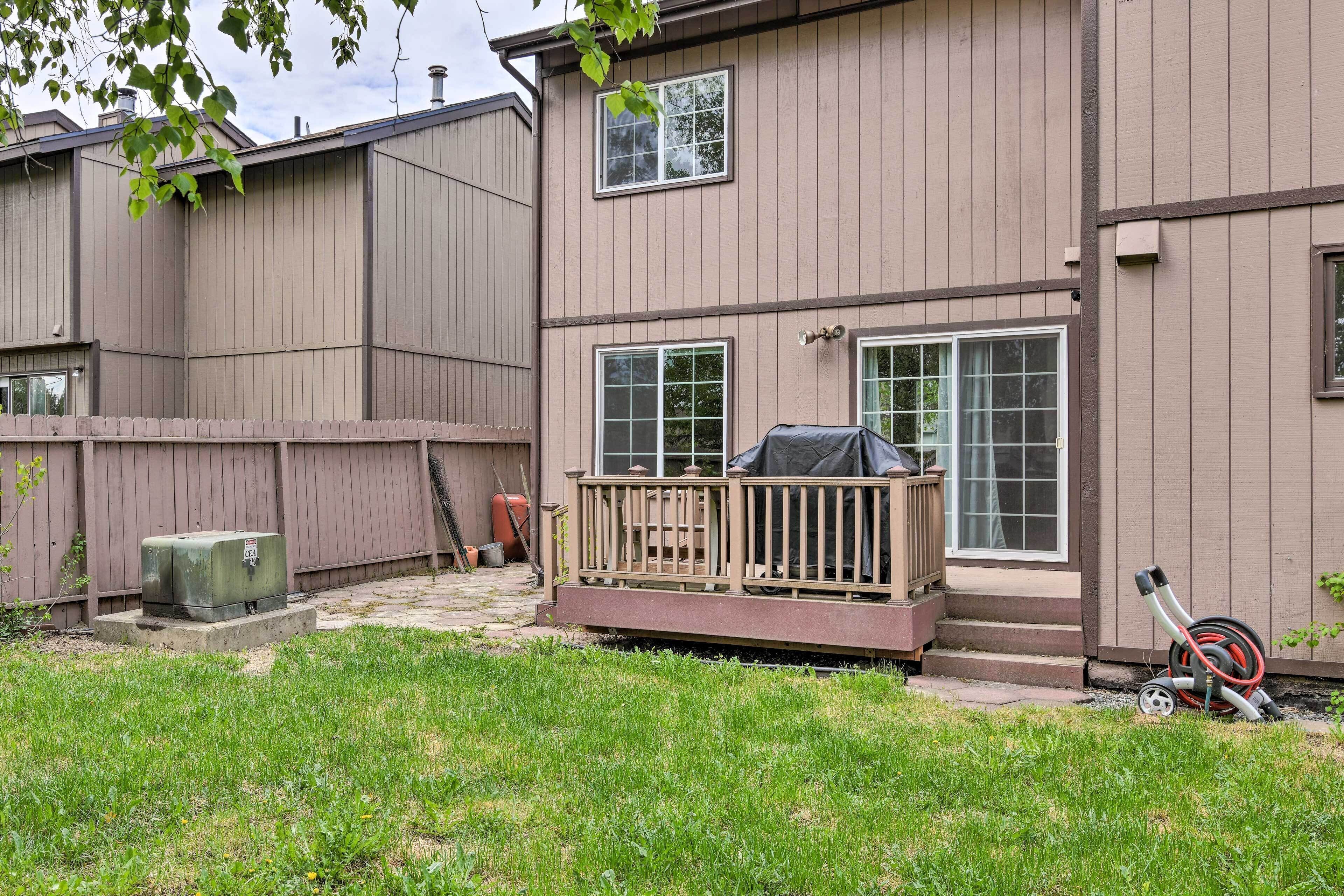 A residential backyard with a wooden deck, a covered grill, and a hose.
