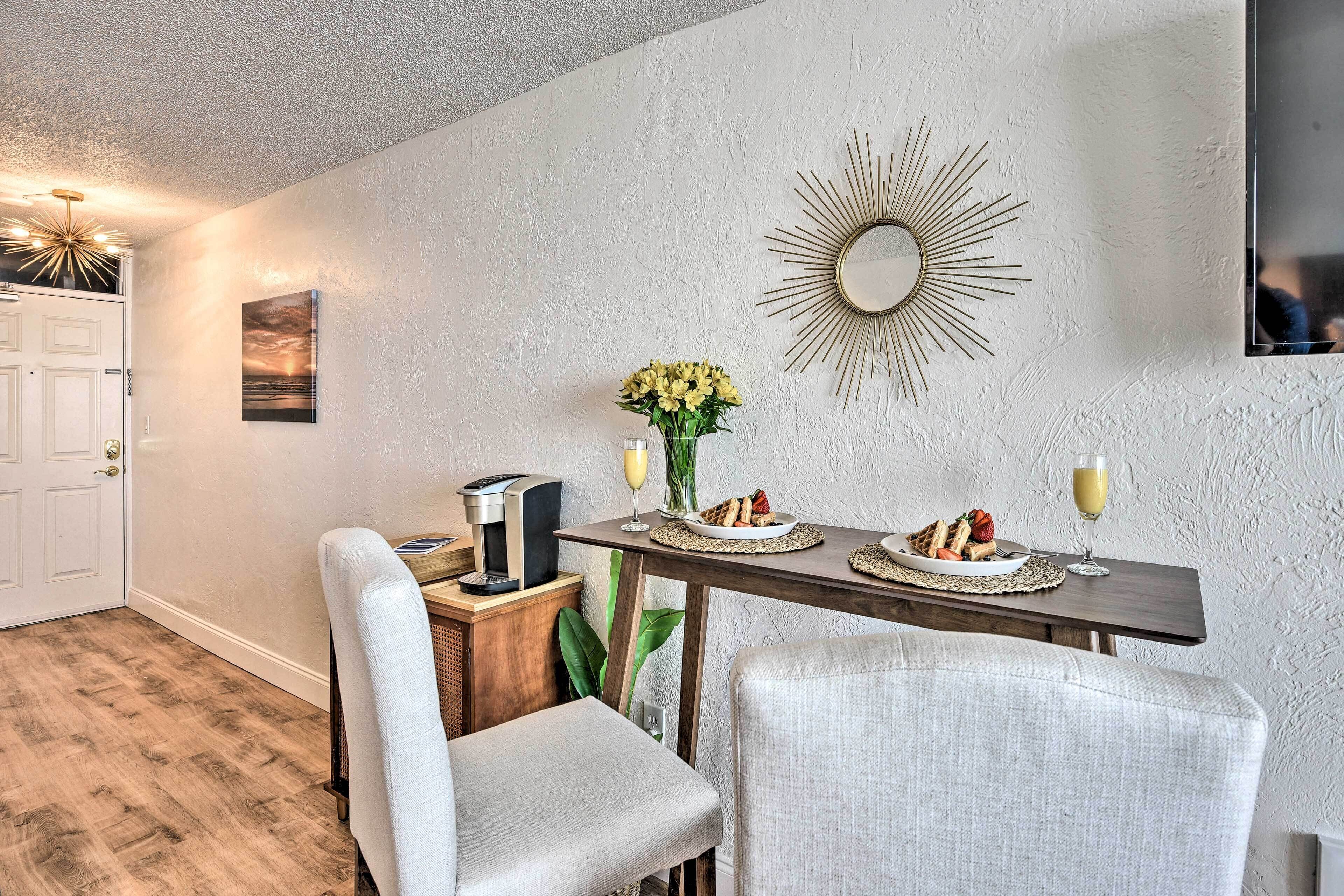 A dining area with a wooden table, two chairs, a coffee machine, and a vase of flowers.