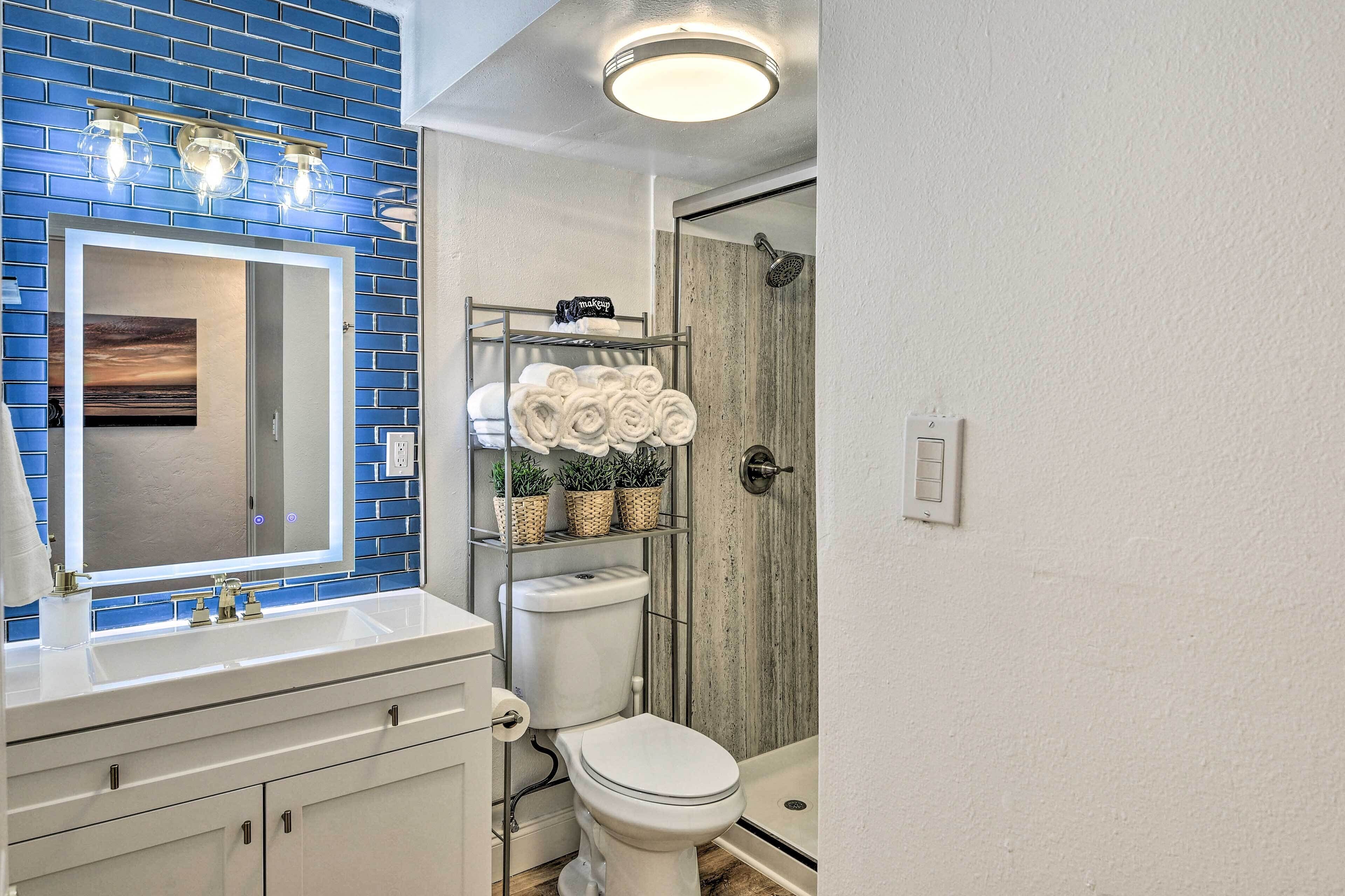 A bathroom with a blue-tiled wall, a white sink, a toilet, and a shower area.
