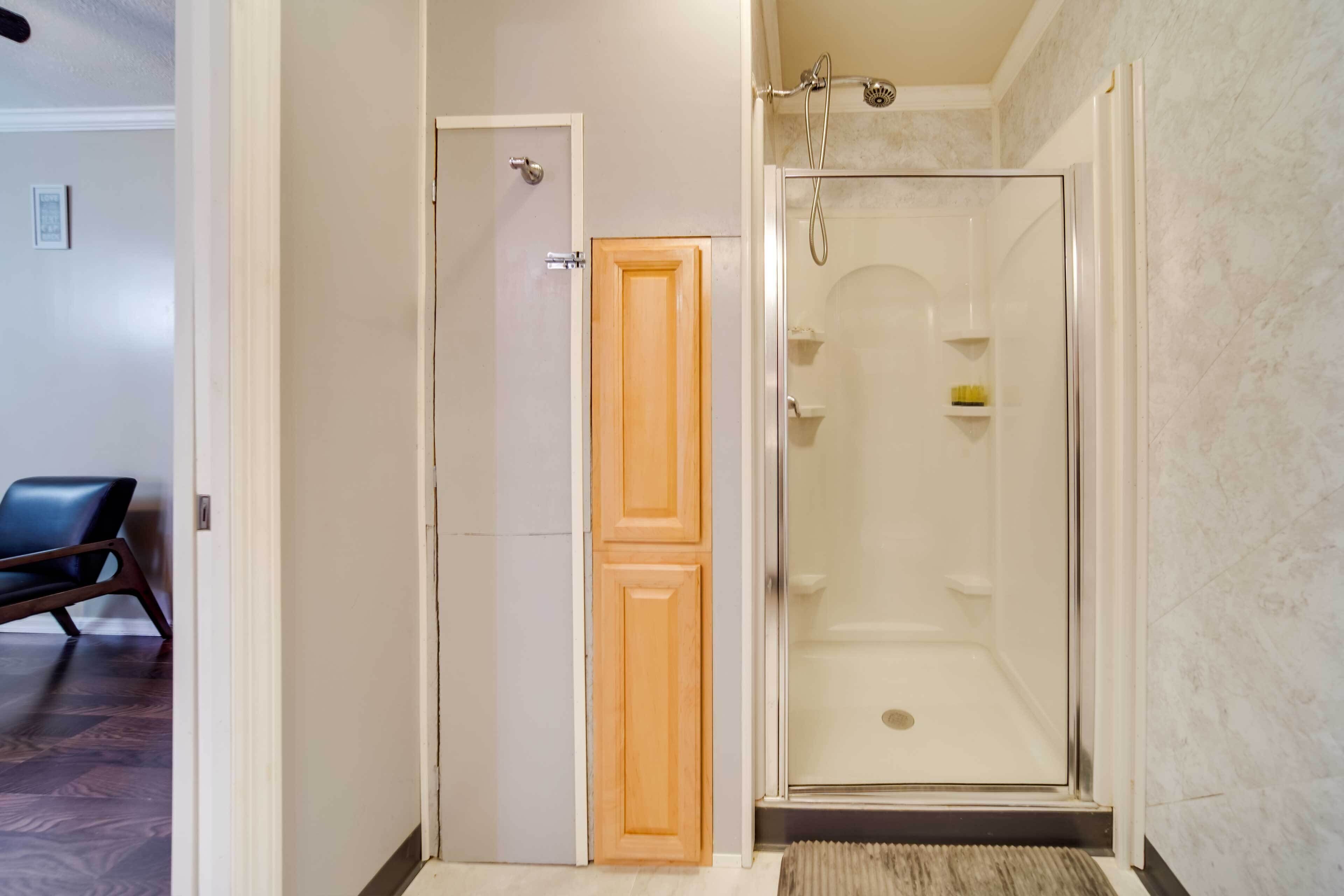 A bathroom with a shower, a wooden door, and a chair in the adjacent room.