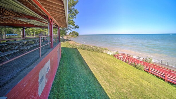Zona esterna coperta con vista sul mare, una zona verdeggiante e una ringhiera rossa.