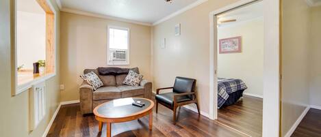 A living room with a wooden floor, a ceiling fan, a sofa, a chair, and a bed.