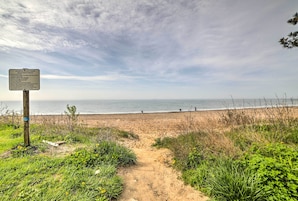 A beach path leading to the ocean with a signboard.