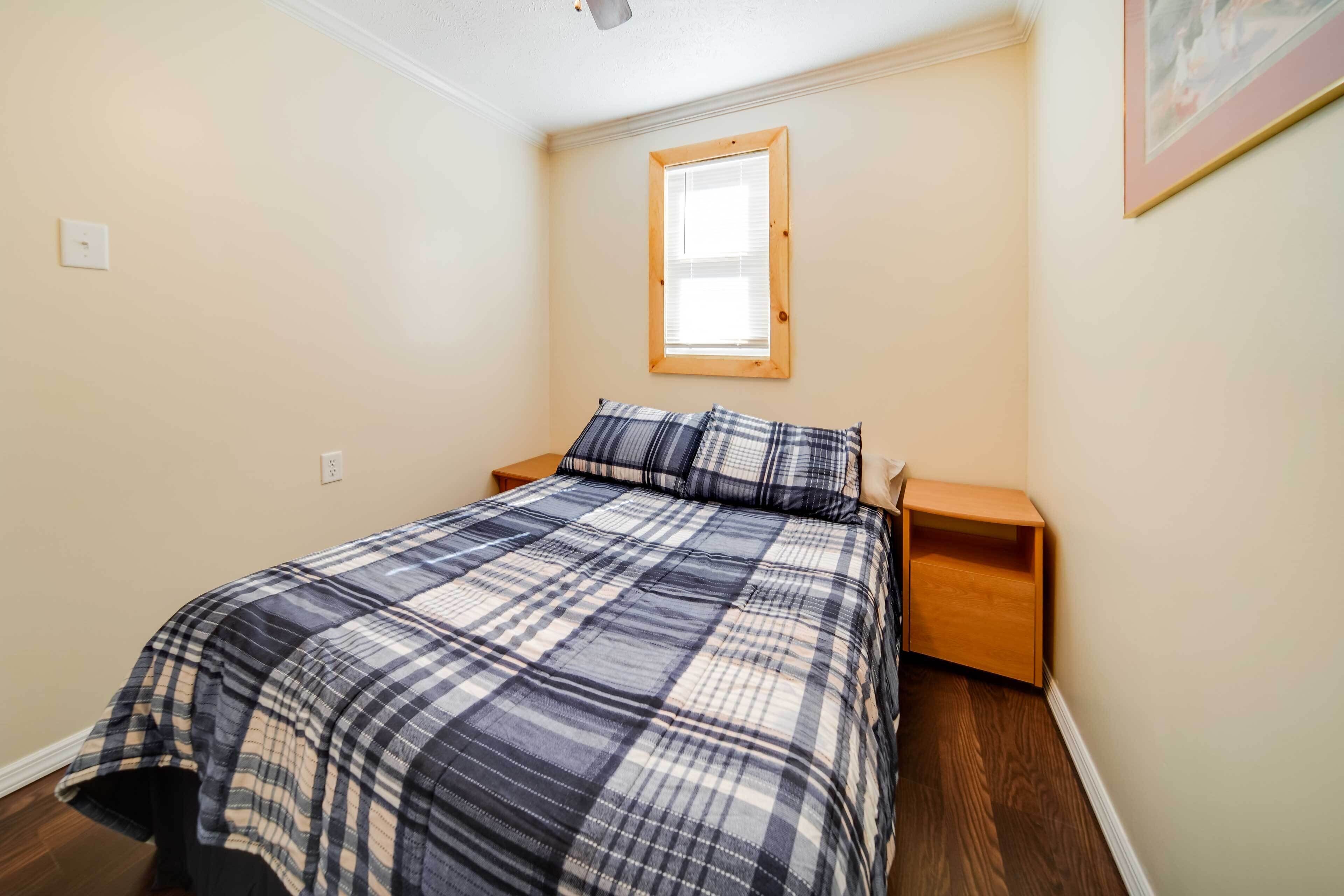 A bedroom with a bed, a nightstand, a wooden headboard, a window, and a light switch on the wall.