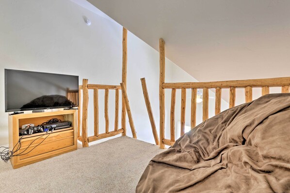 Une chambre à coucher avec un téléviseur posé sur un meuble en bois, un lit recouvert d’une couverture marron et une balustrade en bois.