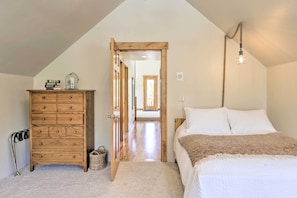 A bedroom with a wooden dresser, a bed with white bedding, and a hanging light fixture.