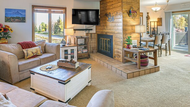 A cozy living room with a fireplace, a television mounted on the wall, and a dining area with chairs and a table.
