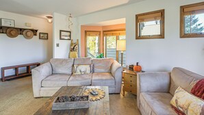 A living room with a beige sofa, a wooden coffee table with decorative items, a wooden side table, and a lamp.