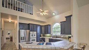 Une cuisine spacieuse avec des meubles de couleur sombre, un grand îlot central doté de tabourets, un ventilateur de plafond et une vue sur l’extérieur.