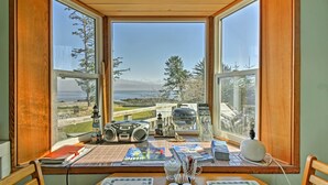 A room with a large window overlooking a scenic view, a wooden table with various items, and a chair.