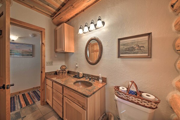A bathroom with wooden cabinets, a granite sink, a mirror, and a framed picture on the wall. - Scenic Riverfront Retreat w/ Hot Tub & Kayaks! (Thompson Falls)