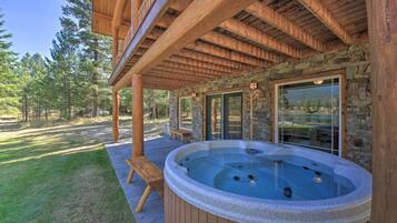 Un jacuzzi bajo una pérgola de madera con paredes de piedra y ventanas amplias.