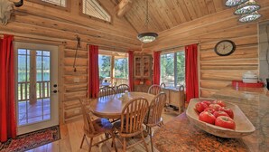 Interior de una cabaña de madera con una mesa de comedor, sillas, un reloj y un cuenco de manzanas.