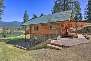 A log cabin with a metal roof, a deck, and a stone foundation. - Scenic Riverfront Retreat w/ Hot Tub & Kayaks! (Thompson Falls)