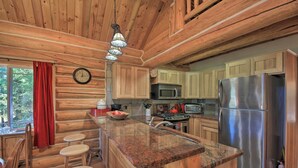 Cocina de cabaña de madera con encimeras de granito, un refrigerador de acero inoxidable y una zona de comedor de madera con taburetes.