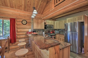 A wooden cabin kitchen with granite countertops, a stainless steel refrigerator, and a wooden dining area with stools.