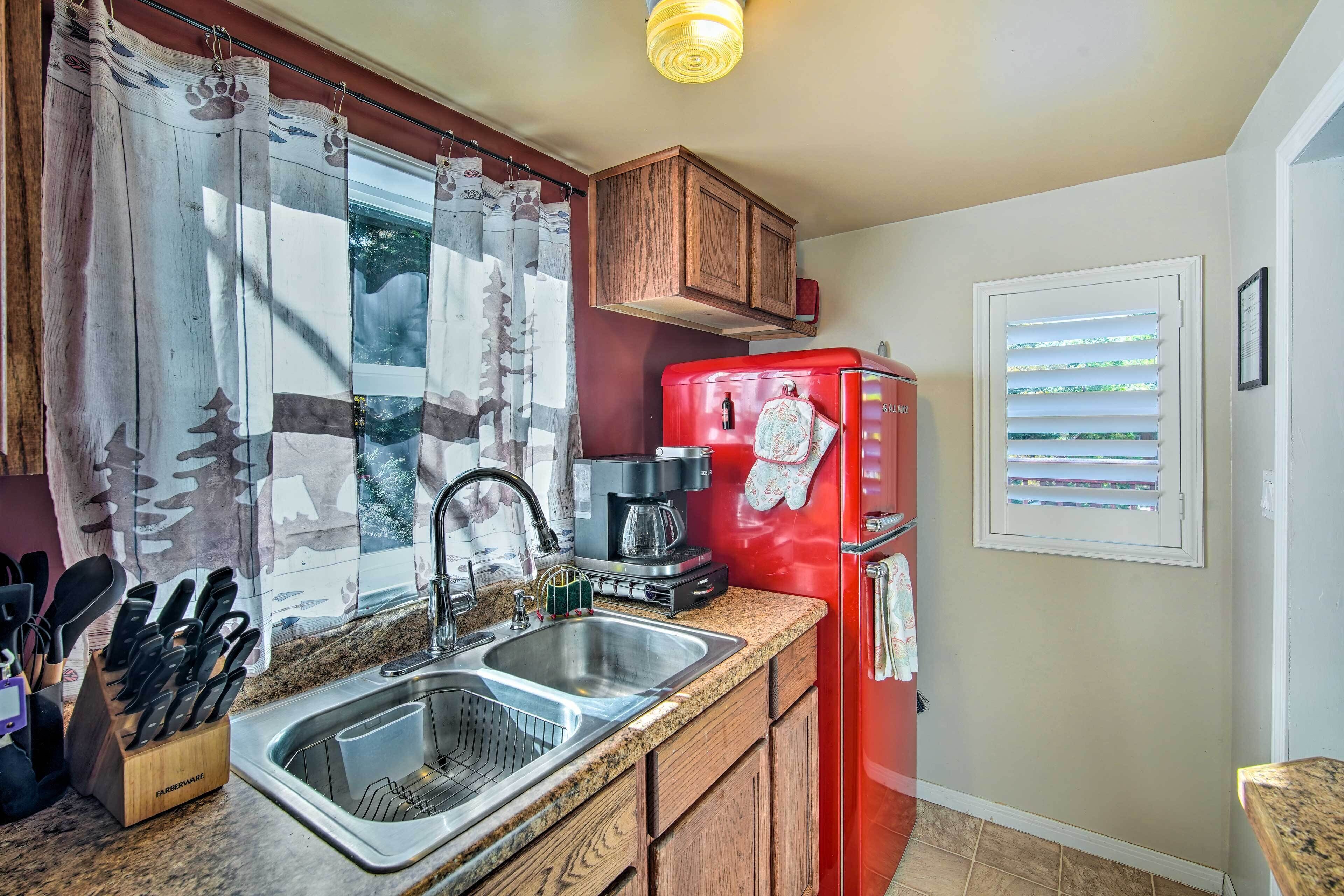 A kitchen with a red refrigerator, stainless steel sink, wooden cabinets, and a window with blinds.
