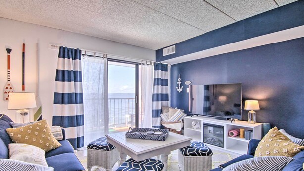Ein wohnzimmer im maritimen Stil mit gestreiften Vorhängen, einem Flachbildfernseher und einem Balkon mit Blick.