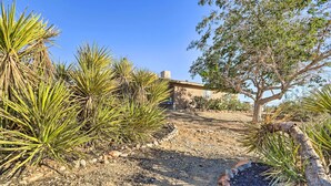 Un paysage désertique avec des plantes de yucca et un arbre, qui mène à un bâtiment à la façade beige et doté d’une cheminée.