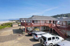 A two-story building with a red balcony, parking area, and a view of the beach. - Rockaway Beach Vacation Rental: Pets Welcome! (Rockaway Beach)