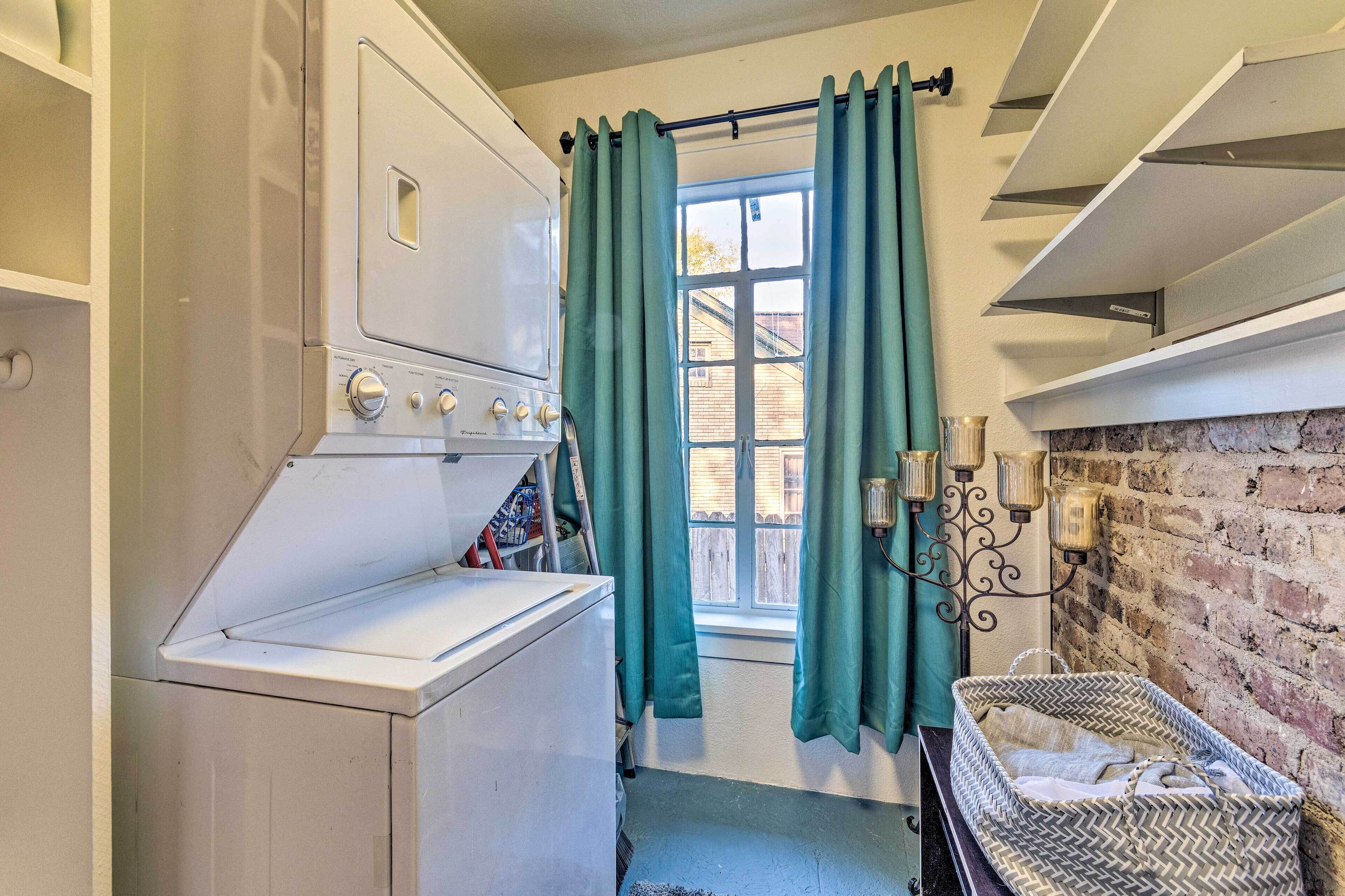 A laundry room with a washing machine, drying racks, and a window with curtains.