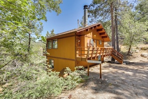 Uma cabana de madeira com escadas para um deck, rodeada por árvores.