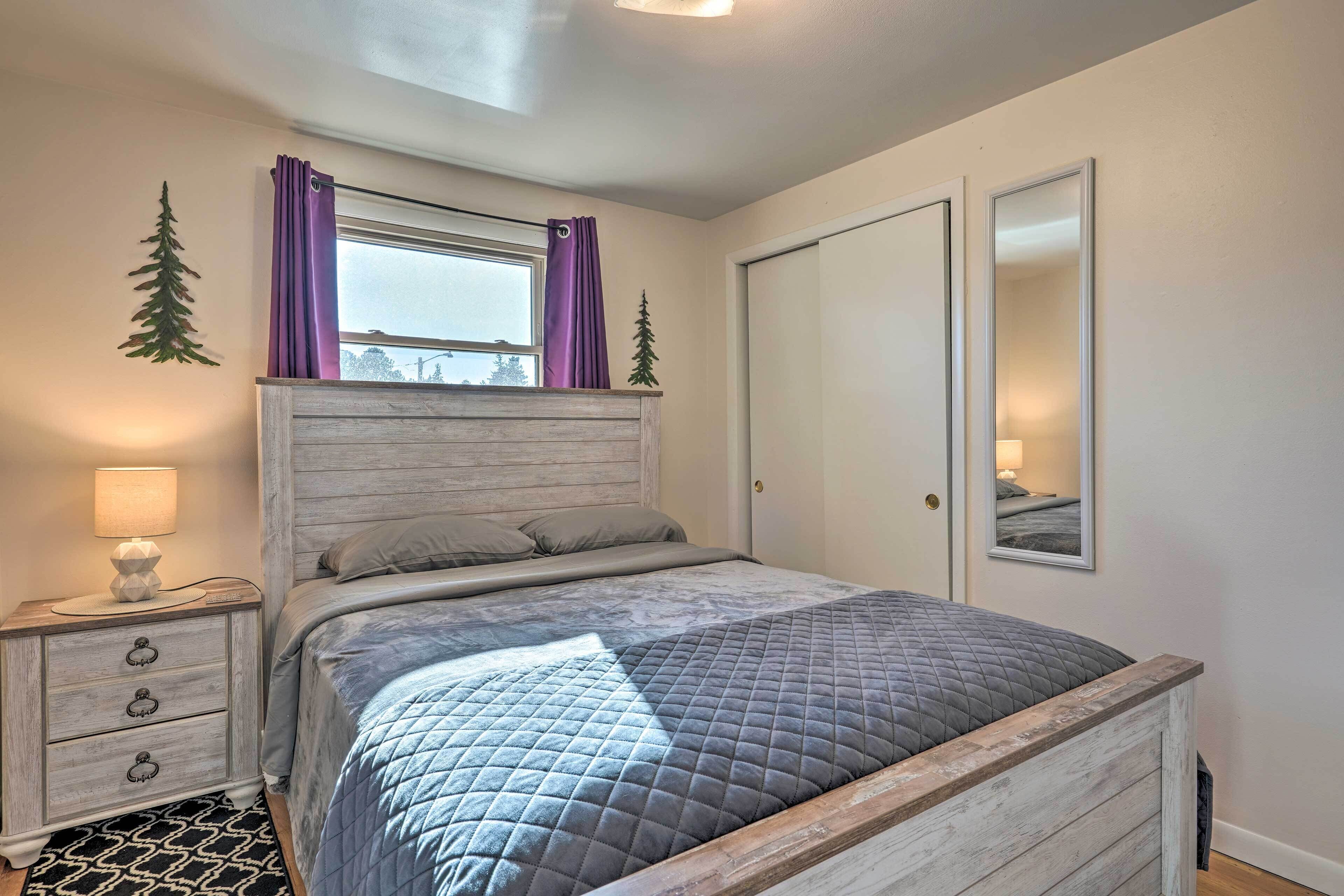 A bedroom with a bed, nightstand, dresser, window with curtains, and a mirror.