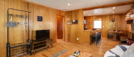 A wooden-floored living room with a television, a coffee table with magazines, and a sofa.