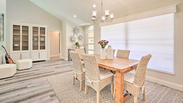 A spacious dining area with a wooden table and wicker chairs, a white cabinet with glass doors, and a large window with blinds. - Luxury Naples Villa - Walk to Vanderbilt Beach! (Naples)