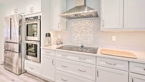 A modern kitchen with stainless steel appliances, white cabinetry, and a patterned backsplash. - Luxury Naples Villa - Walk to Vanderbilt Beach! (Naples)