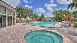 A swimming pool with a hot tub, surrounded by lounge chairs and umbrellas, with palm trees and a building in the background. - Luxury Naples Villa - Walk to Vanderbilt Beach! (Naples)