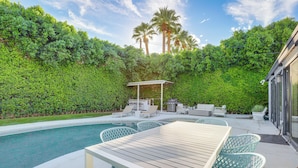 A poolside area with a wooden table and chairs, a barbecue grill, and a covered seating area. - 1 Mi to Dtwn Palm Springs: Home w/ Fire Pit! (Palm Springs)