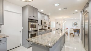 A modern kitchen with stainless steel appliances, a marble countertop, and a dining area with a table and chairs. - 1 Mi to Dtwn Palm Springs: Home w/ Fire Pit! (Palm Springs)