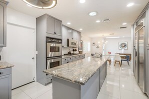 A modern kitchen with stainless steel appliances, a marble countertop, and a dining area with a table and chairs. - 1 Mi to Dtwn Palm Springs: Home w/ Fire Pit! (Palm Springs)