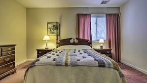 Een slaapkamer met een groot bed, twee nachtkastjes met lampen, een kaptafel, een raam met gordijnen en een schilderij aan de muur.
