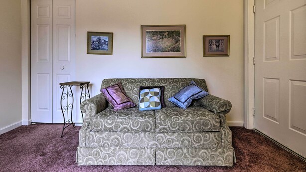 Een woonkamer met een gestreept bankje, drie ingelijste foto's aan de muur, een bijzettafeltje en een deur.