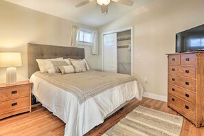 Quarto com cama, cómoda de madeira, mesa de cabeceira, ventoinha no teto e guarda-roupa.