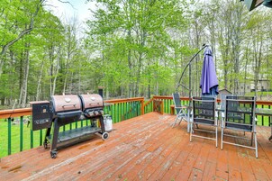 Una terraza de madera con una parrilla, sillas y una mesa.