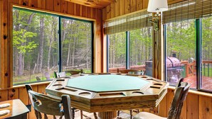 A wooden interior with a large octagonal table, wooden chairs, and large windows offering a forest view. - Peaceful Wooded Retreat at Lake Wallenpaupack! (Lake Ariel)