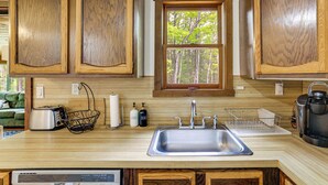 A kitchen with wooden cabinets, a window, a sink, a toaster, and a coffee maker. - Peaceful Wooded Retreat at Lake Wallenpaupack! (Lake Ariel)