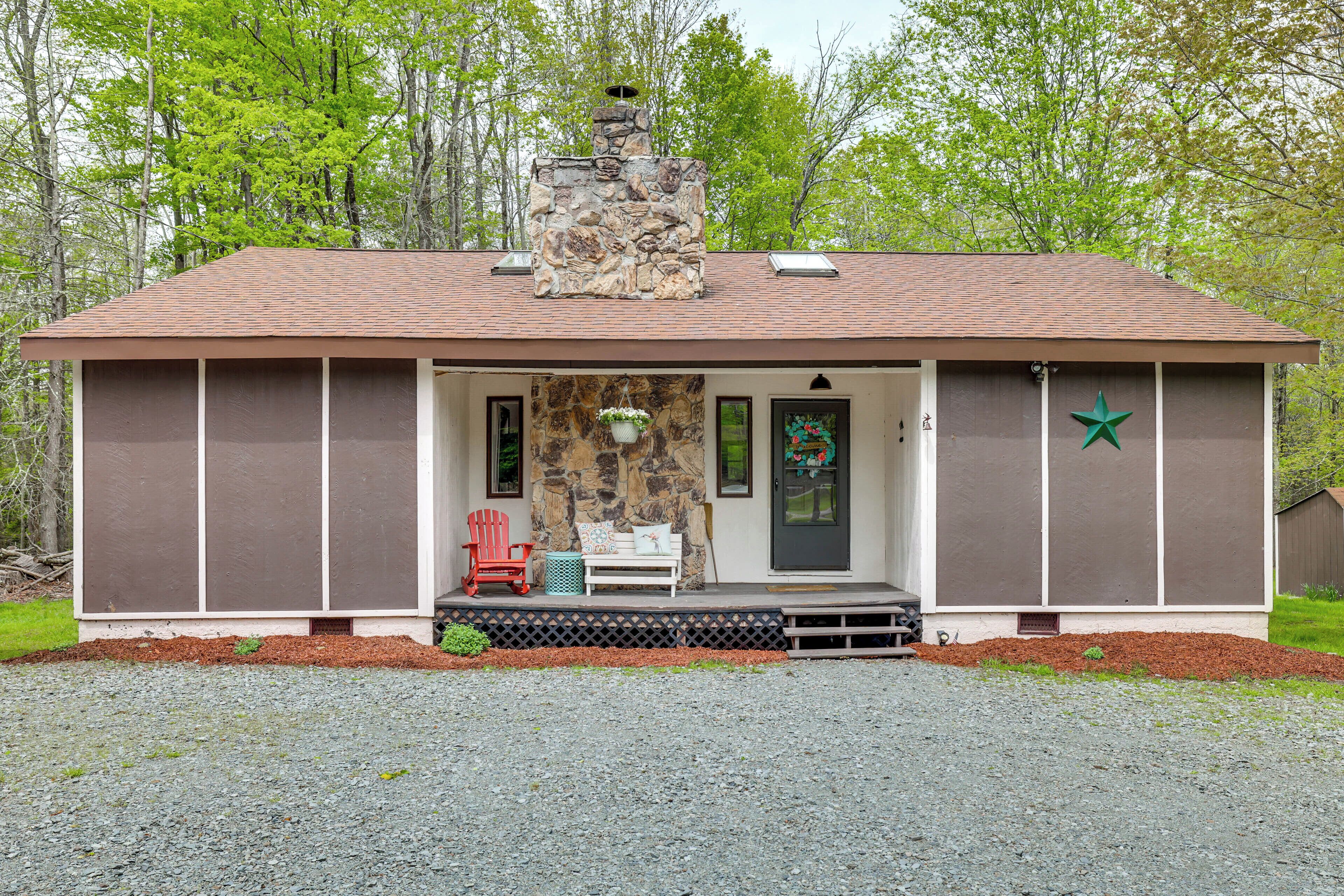 A small, single-story building with a stone chimney, a front porch with a bench and a red chair, and a green star decoration on the door.