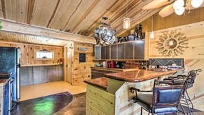 A rustic kitchen with wooden walls and a bar area with stools. - Waterfront Home w/ 3 Decks on Lake of the Ozarks! (Sunrise Beach)